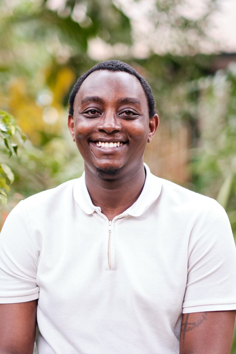 Lawrence Muthoga smiling, in a white polo shirt outdoors